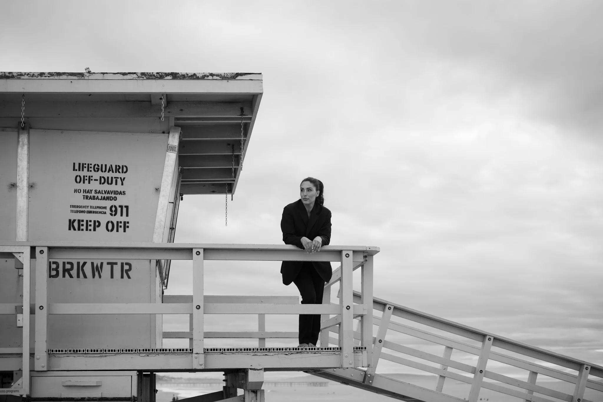A woman in an elegant outfit poses on a white lifeguard tower at the beach