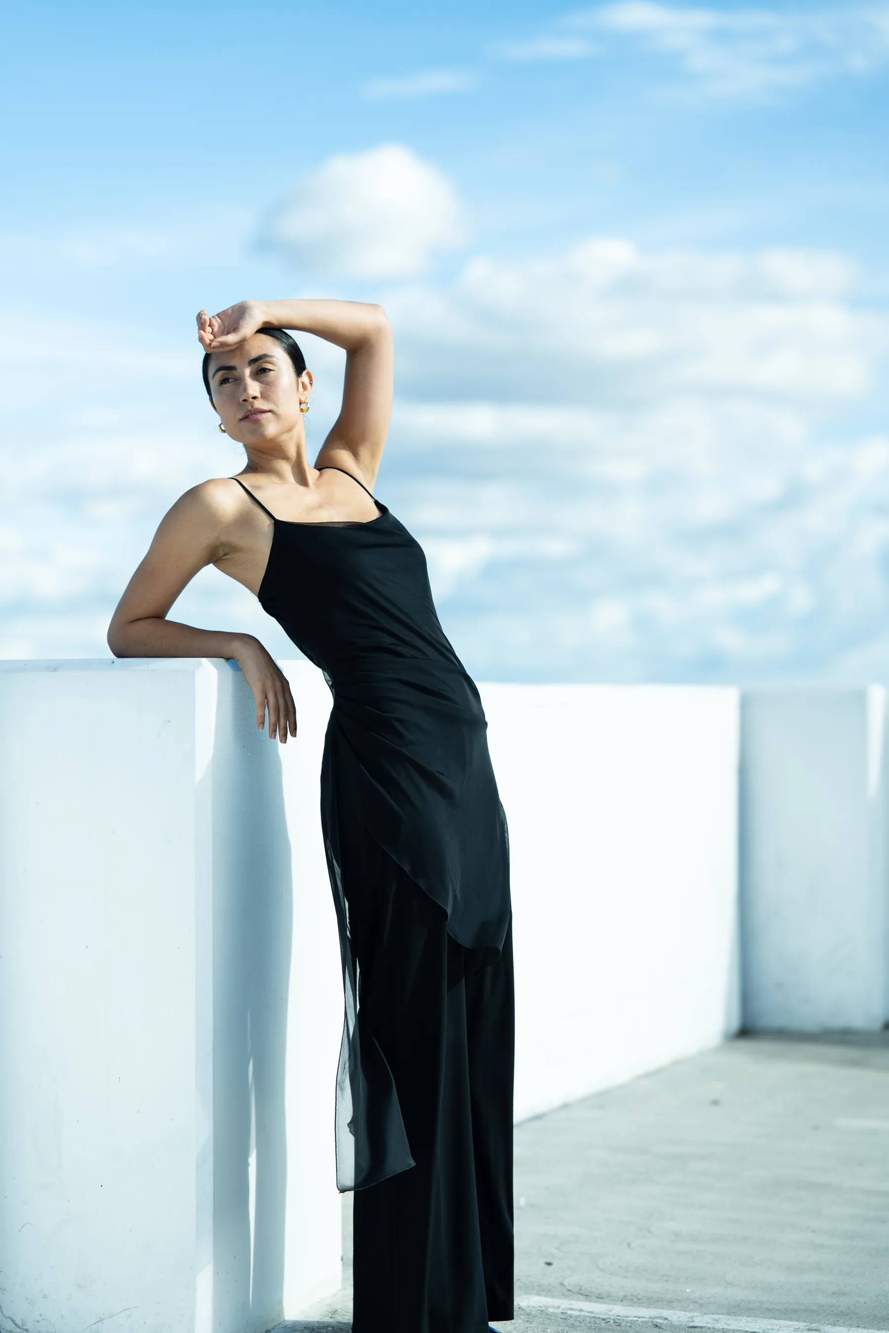 Fashion portrait on urban rooftop, model in structured black outfit, natural daylight creating soft shadows, contemplative mood